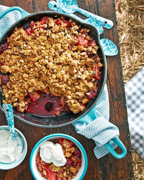 apple blackberry crumble in an enamel cast iron skillet with some scooped into a bowl with sour cream whip on top