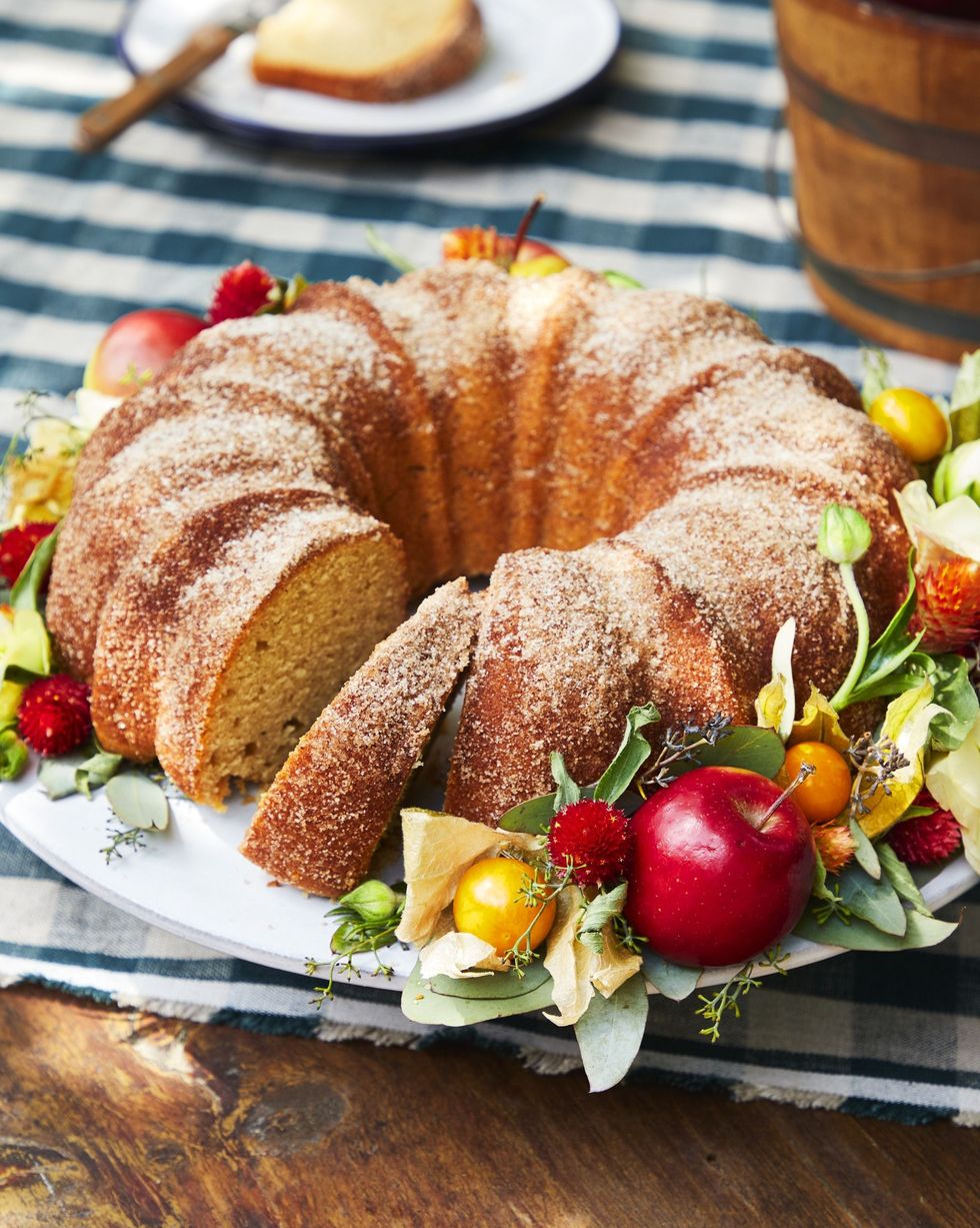 apple cider donut bundt cake on a plate with apples and lemons and flours around it for garnish