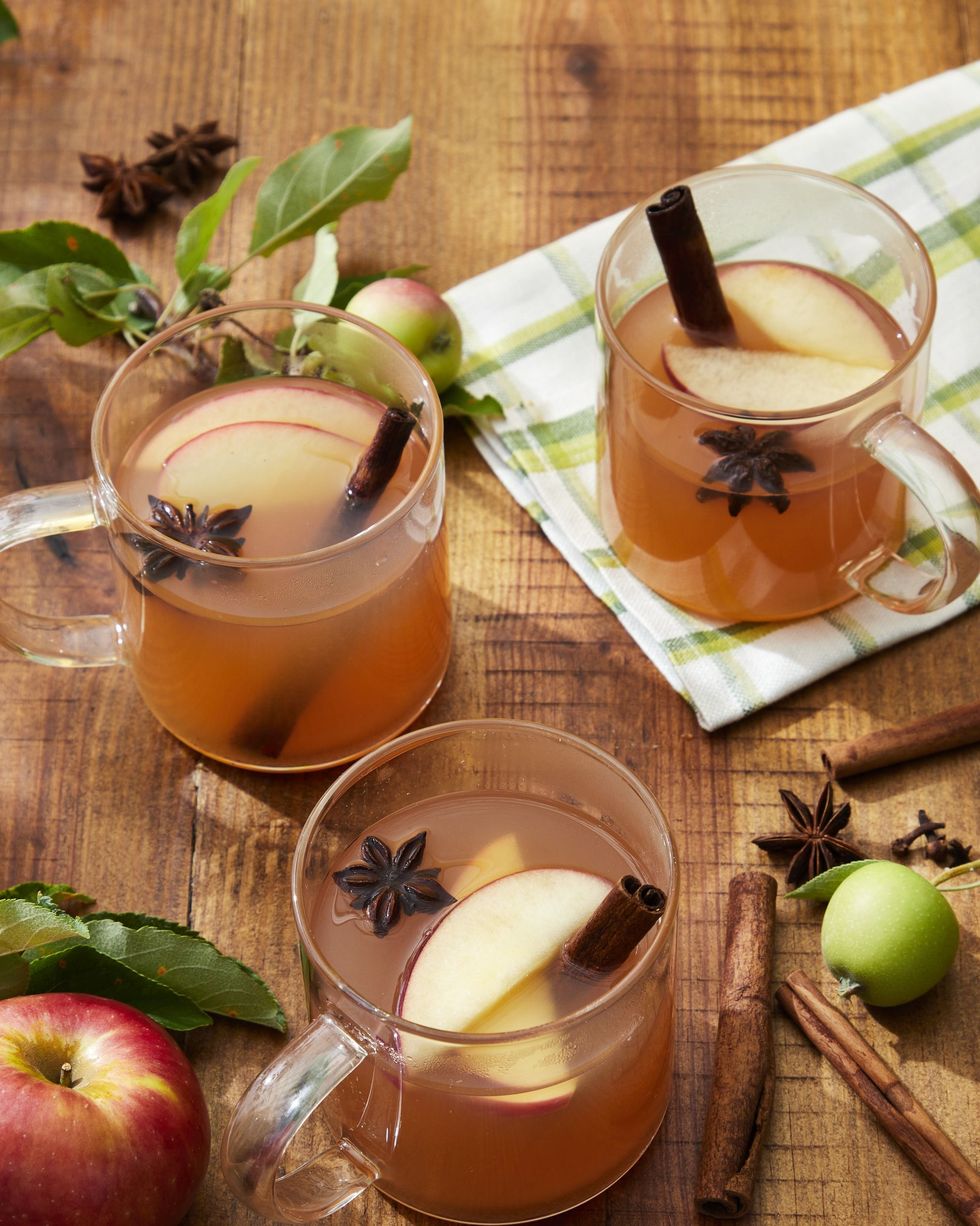 three glass mugs of woodchuck warmer apple cider cocktail with cinnamon sticks star anise and slices of apple as garnish