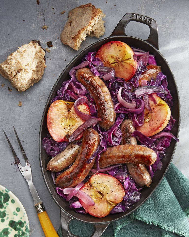 seared sausage with cabbage and pink lady apples in an oval cast iron baking pan
