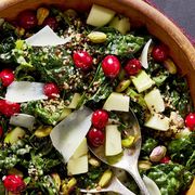 kale salad with pickled cranberries and crispy quinoa in a wooden serving bowl topped with apple chunks and shaved manchego