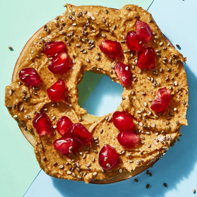 closeup of a cored apple slice with almond butter and pomegranate, a healthy sweet snack