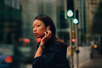 a woman wears an apple watch series 10 and apple earphones while waiting to cross a busy city street
