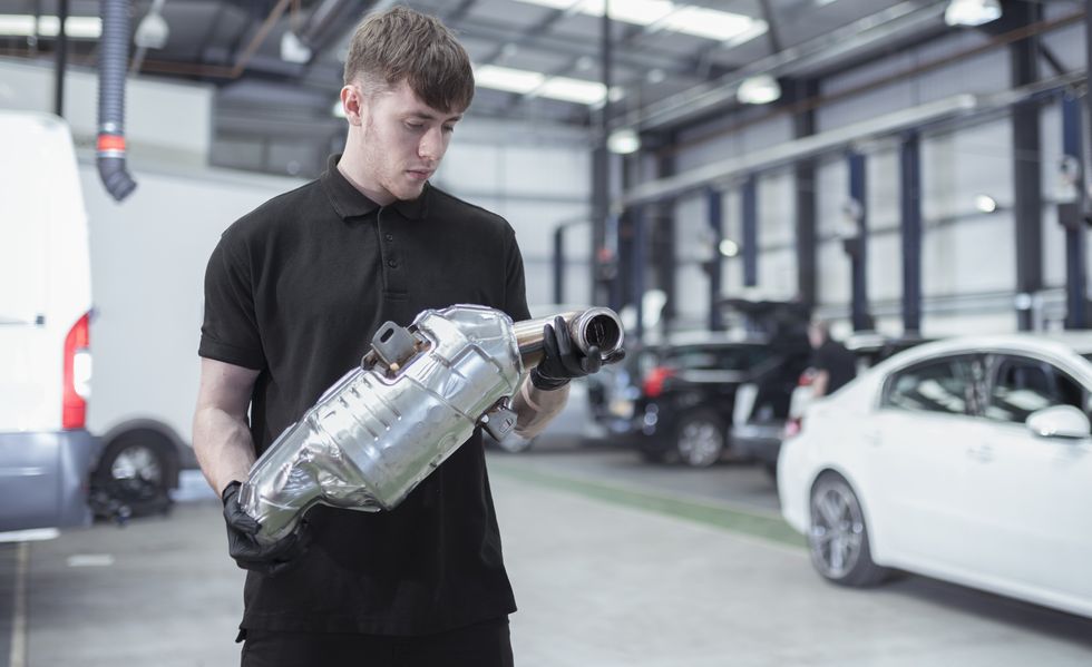 apprentice holding catalytic converter in car service centre