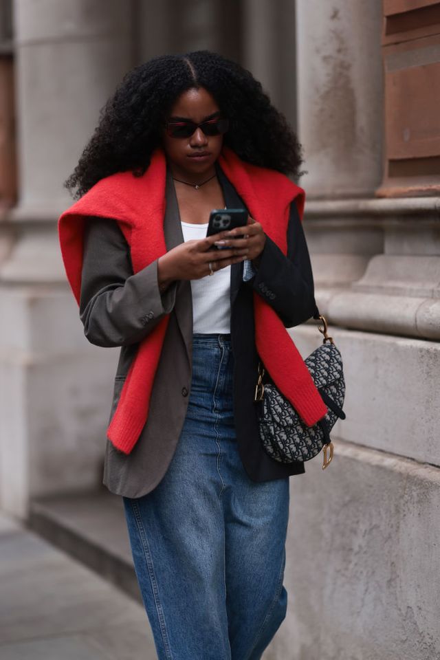 london fashion week girl on her phone wearing a blazer and red jumper on top with mid blue jeans and christian dior bag