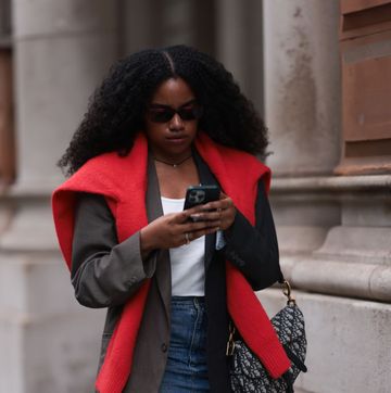 a girl at london fashion week wearing a red jumper over a blazer and a white top whilst on her phone
