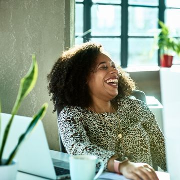 attractive businesswoman in animal print blouse, sitting at desk in modern office, head back, smiling and cheerful, eyes closed, curly hair, joy, carefree
