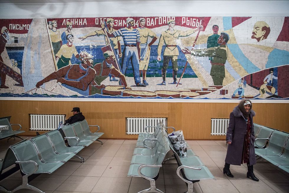 Reizigers wachten in Aral op een trein onder een mozaek uit de Sovjettijd