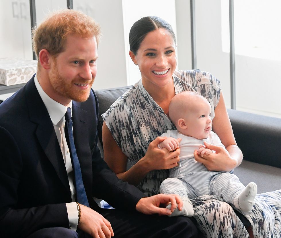 Prince Harry, Meghan Markle and their young son, Archie, during a trip of Africa. Archie is sat on Meghan's lap and the parents are both smiling.