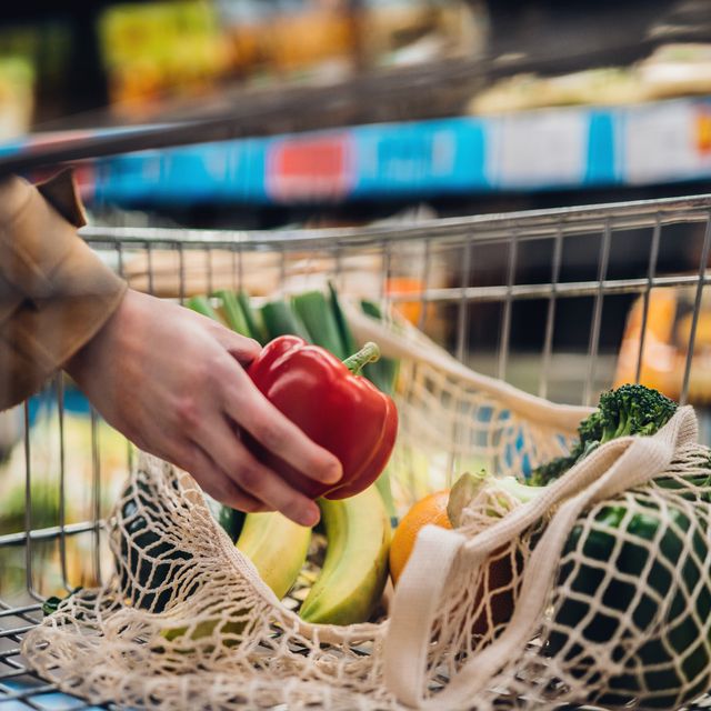 woman in supermarket putting pepper in shopping basket