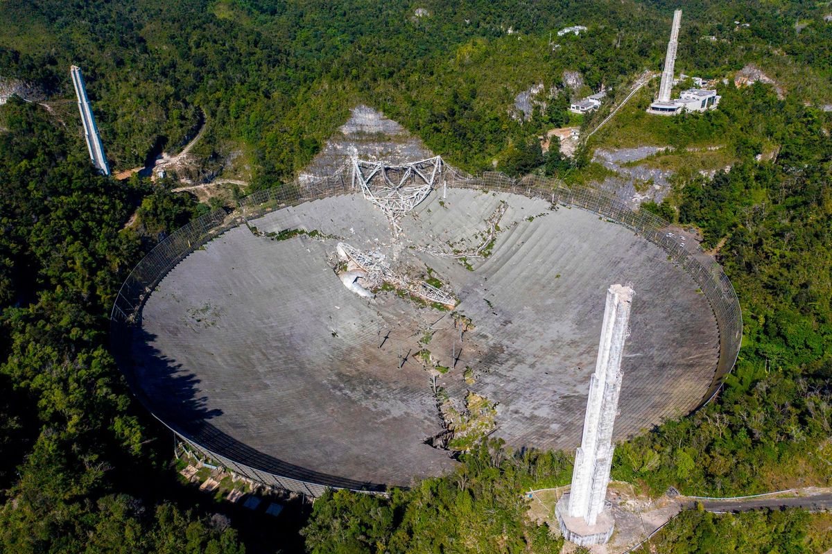 Op deze luchtfoto is de schade te zien die aan het Arecibo Observatory werd aangericht toen het negenhonderd ton zware instrumentenplatform boven de telescoop losschoot tegen een rotswand werd geslingerd en op de schotelantenne eronder stortte