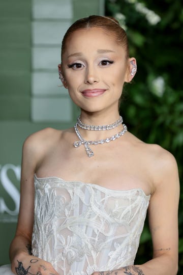 ariana grande smiles at the camera, she wears a strapless white gown and crystal jewelry