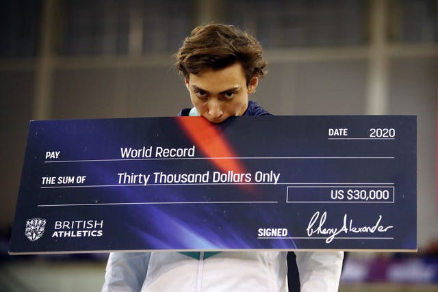 Armand Duplantis sostiene un cheque tras conseguir el récord del mundo de salto con pértiga.