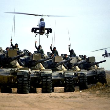1974 us army soldiers give hand signals from m60 main battle tanks during a field training exercise two ah 1 cobra helicopters are hovering overhead