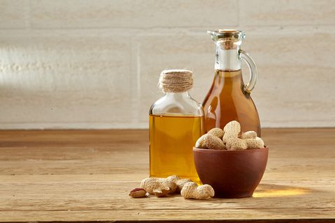 Aromatic oil in a glass jar and bottle with peanuts in bowl on wooden table, close-up.