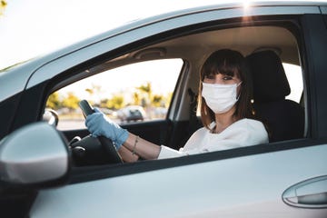 mujer joven al volante de su coche con mascarilla y gauntes