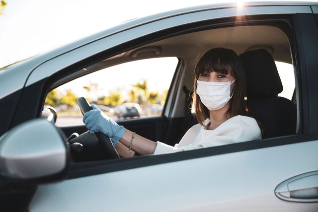 mujer joven al volante de su coche con mascarilla y gauntes
