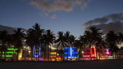 art deco district, miami beach shows colorful retro neon signs with palm trees and clouds on beach, florida