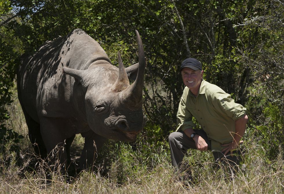 Art Wolfe, photographer kneeling next to a white rhinoceros in Kenya.