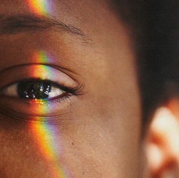 half of a black womans face with a rainbow light reflection over her eye