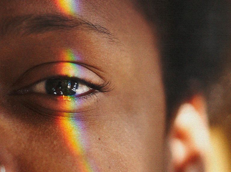 half of a black womans face with a rainbow light reflection over her eye