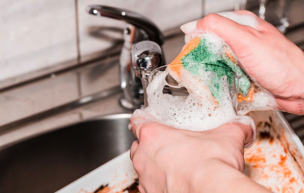 woman cleaning glass in sink with kitchen sponge
