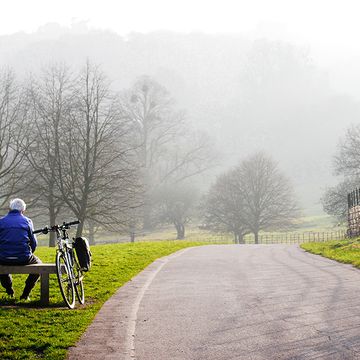 older cyclist sitting on park bench next to bike