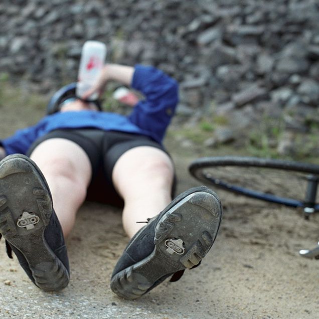tired cyclist lying down on the ground next to bike, drinking from a water bottle