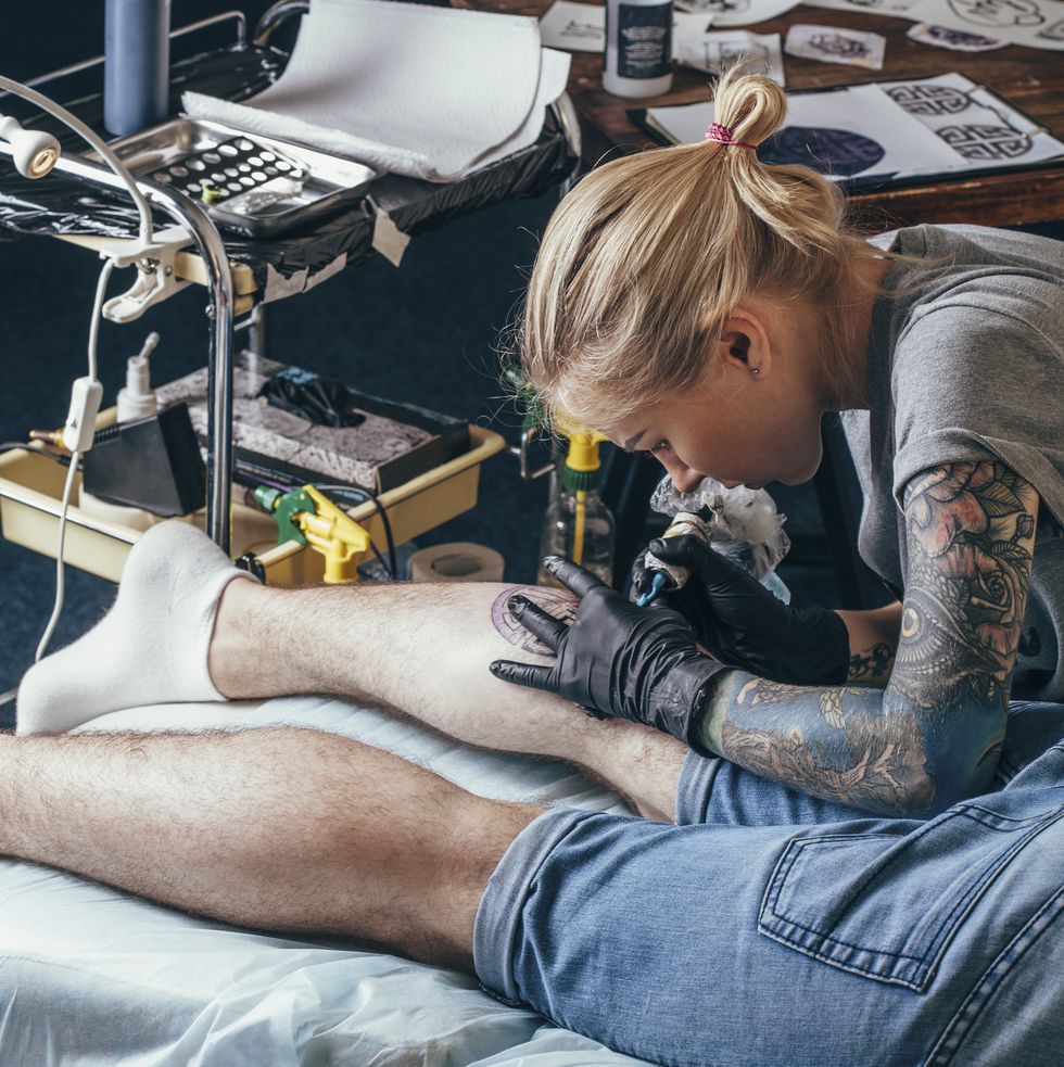 artist tattooing design on mans leg at studio