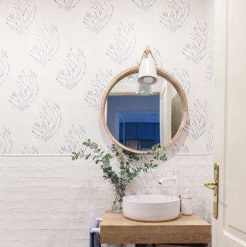baño con azulejos blancos tipo metro, papel pintado con dibujos de corales azules y mueble de madera volado