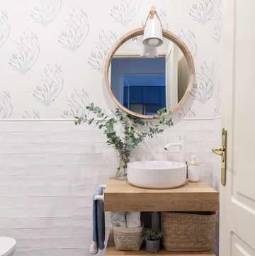 baño con azulejos blancos tipo metro, papel pintado con dibujos de corales azules y mueble de madera volado