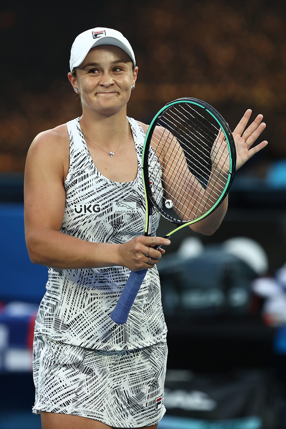 ash barty, holding a tennis racket in her right hand, waves to fans during a tennis game