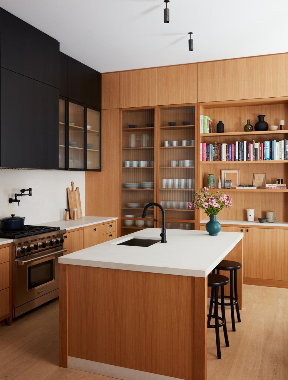 a kitchen with wood floors and shelves and black cabinets with a white island countertop