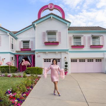 host ashley graham poses in front of the finished barbie dream house, as seen on barbie dream house challenge, season 1
