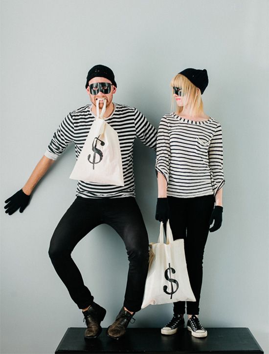 a couple both wearing black pants striped black and white shirts black masks black gloves and hats and carrying bags with a big black dollar sign on them