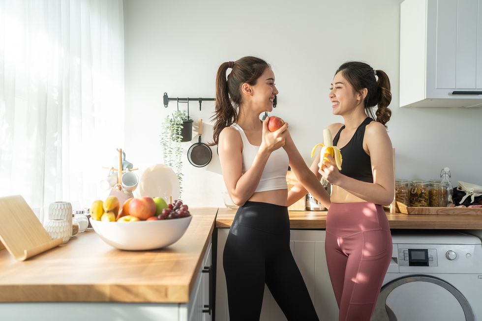 asian active two women sibling in sportswear eat an apple in kitchen young beautiful girl sister feeling happy and enjoy eating fruits healthy foods to diet and lose weight for health care in house