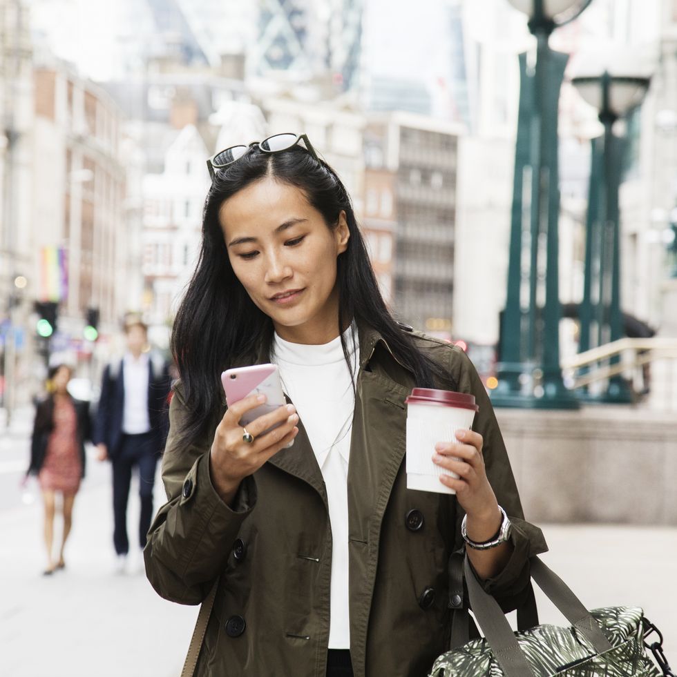 asian businesswoman looks at smart phone while walking in city