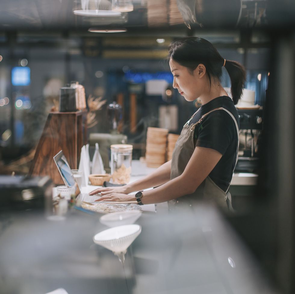 asian chinese female barista using laptop while enjoying dinner at coffee shop bar counter