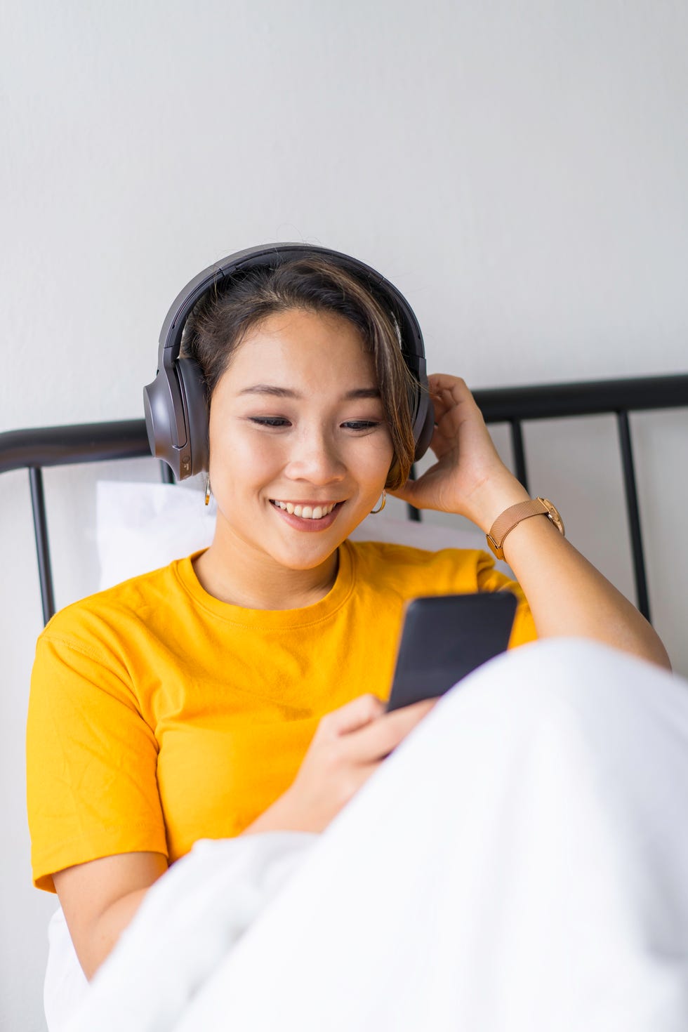 virtual happy hour ideas - Asian girl enjoying music on bed with smart phone