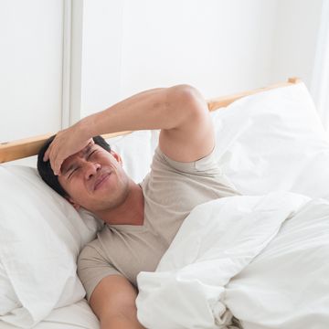 asian man on the bed and hand on forehead illness, stress, headache caused by overworking or hard work a man sleeping on the bed with a headache