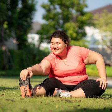 asian overweight woman exercising stretch alone in public park in village, happy and smile in morning during sunlight fat women take care of health and want to lose weight concept