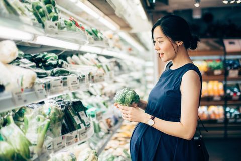 Asian pregnant woman grocery shopping at the vegetable aisle in supermarket