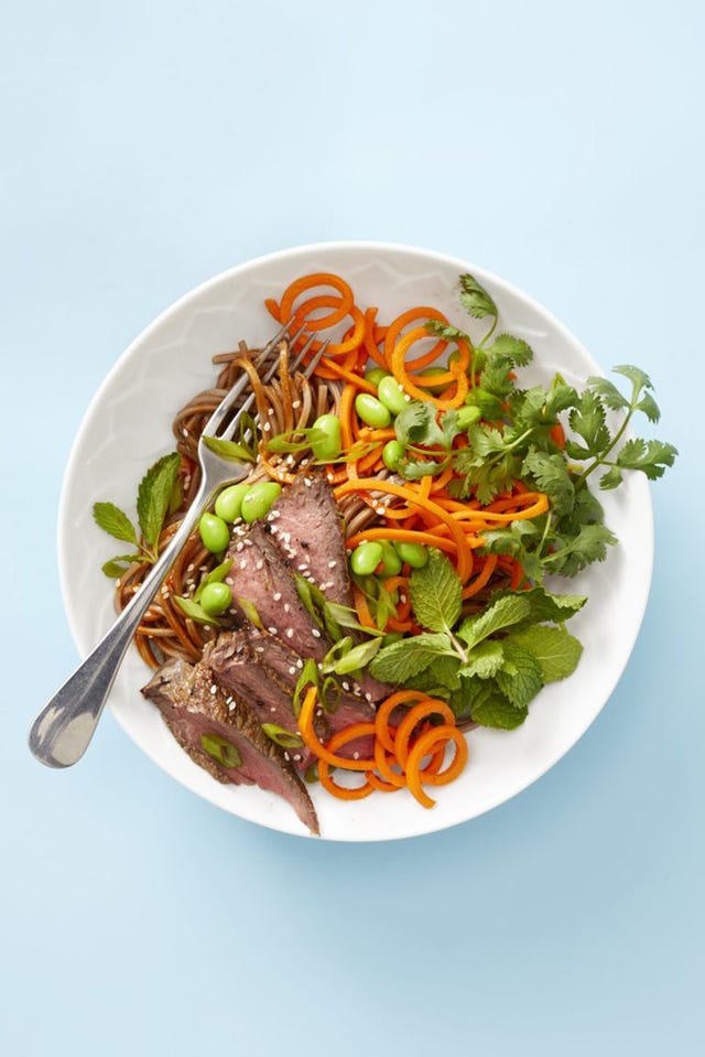 asian steak noodle bowl on a blue background with a fork