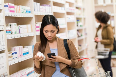 asian woman checking supplement on smartphone at pharmacy