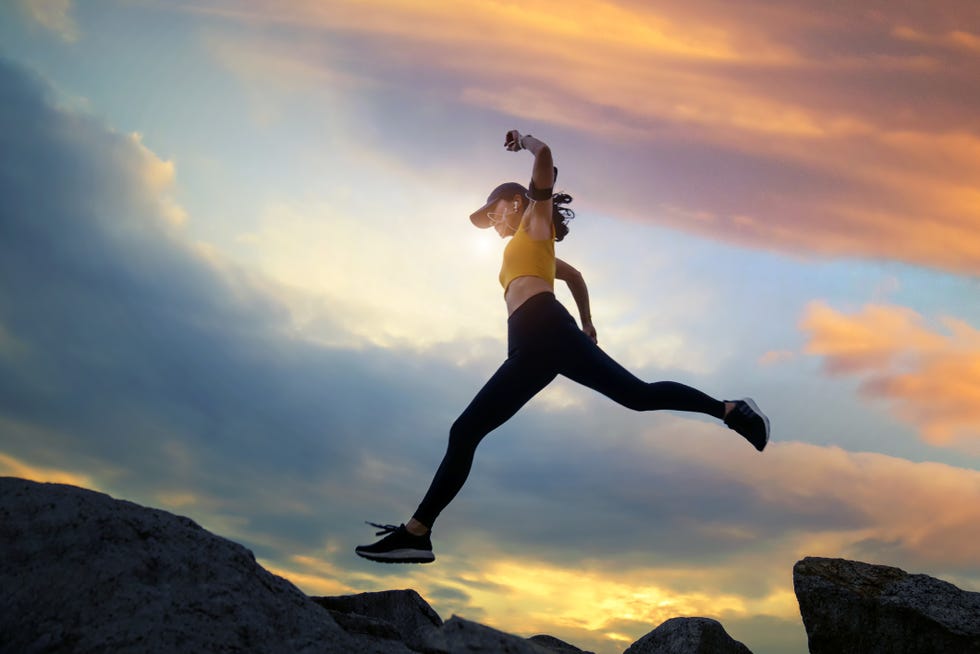 asian woman runs and jumping on mountain ridge at sunset