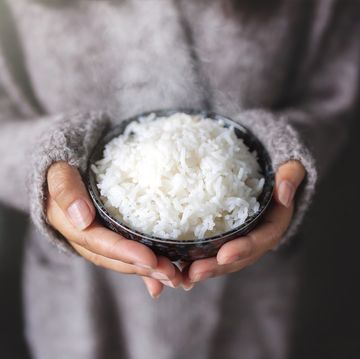 asian women holding cooked jasmine rice bowl wearing a gray sweater
