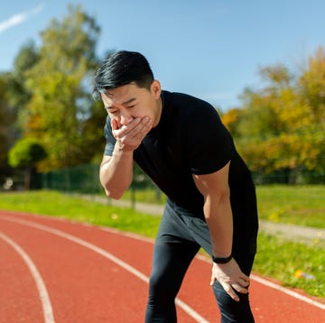 Asian young man doing sports at the stadium. He stands bent over on the treadmill, covers his mouth with his hand, feels very nauseous hardloper wordt misselijk tijdens zijn training