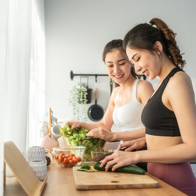 asian young two women sibling in sportswear cooking salad in kitchen active beautiful girl sister feel happy and enjoy eating vegetables healthy foods to diet and lose weight for health care in house