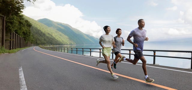 group of three people running along a scenic lakeside road