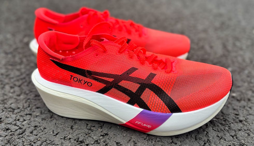 a pair of red and black asics racing shoes on tarmac